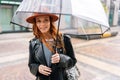 Medium shot of elegant young woman in stylish hat standing with transparent umbrella on city street enjoying rainy Royalty Free Stock Photo