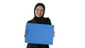 Smiling Arab woman in hijab holding blank blue poster and lookin Royalty Free Stock Photo