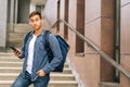 Medium shot of handsome delivery man with large thermo backpack holding using mobile phone standing on stairs of office