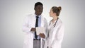 Intellectual healthcare professional afro american doctor with collegue using digital tablet on gradient background. Royalty Free Stock Photo