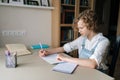 Medium shot of little child schoolgirl writing in exercise book doing some homework, sitting at table near window. Royalty Free Stock Photo