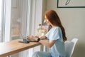 Medium shot portrait of beautiful happy young woman typing on laptop computer sitting at table by window in cafe Royalty Free Stock Photo