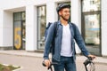 Medium shot portrait of cheerful handsome young delivery man in protective helmet standing near bicycle in city street Royalty Free Stock Photo