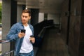 Medium shot portrait of confident young man using typing mobile phone, standing on balcony terrace with coffee coffee Royalty Free Stock Photo