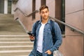 Medium shot portrait of handsome delivery man with thermo backpack holding using mobile phone standing on stairs of Royalty Free Stock Photo