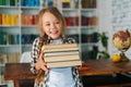 Medium shot portrait of joyful elementary child school girl holding stack of books in library at school, looking at Royalty Free Stock Photo