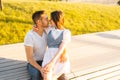 Medium shot portrait of loving young couple hugging and kissing sitting on bench in city park in summer sunny day. Royalty Free Stock Photo