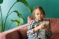 Medium shot portrait of pretty adorable little child girl using smartphone looking at camera, watching cartoons,