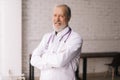 Medium shot portrait of smiling mature male doctor in white lab coat posing with crossed arms Royalty Free Stock Photo