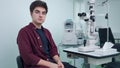 Medium shot portrait of young Caucasian man sitting in ophthalmologic clinic at retina camera posing. Handsome serious