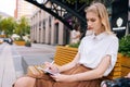 Medium shot of serious young woman writing creative ideas in notepad sitting outdoors on bench. Skilled female artist Royalty Free Stock Photo