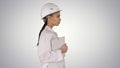 Attractive Hispanic woman in white lab coat and white safety hard hat walking holding notebook or tablet on gradient Royalty Free Stock Photo