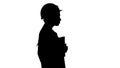 Silhouette Attractive Hispanic woman in white lab coat and white safety hard hat walking holding notebook or tablet. Royalty Free Stock Photo