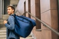 Medium shot of smiling handsome young male of food delivery service with large thermo backpack standing posing in office