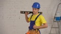 Medium shot of a smiling young construction worker wearing a tool belt, holding a construction water level on his Royalty Free Stock Photo