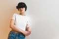 Medium shot of a woman with black strip on her eyes, wearing white top and jeans and leaning against a white wall Royalty Free Stock Photo