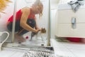 Medium shot of a woman in a red top showering a cat in a bathroom shower, taken from the side. Royalty Free Stock Photo