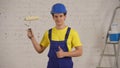 Medium shot of a young construction worker standing in the room under renovation with a roller in his hand, giving a Royalty Free Stock Photo