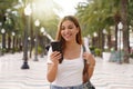 Medium shot young smiling woman uses smartphone reads news from social networks searches text sends mails online strolls at street