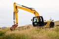 Medium size yellow excavator working in a green field. Building family house or farm in a country side concept. Dramatic cloudy