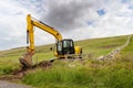 Medium size yellow excavator working in a green field. Building family house or farm in a country side concept. Dramatic cloudy