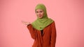 Medium-sized isolated photo capturing an attractive young woman wearing a hijab, veil. She is pointing her hand to the