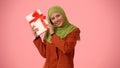 Medium-sized isolated photo capturing an attractive young woman wearing a hijab, veil. She is shaking a gift box