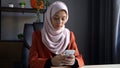 Medium-sized photo capturing an attractive young woman wearing a hijab, veil. She is holding a smartphone, typing