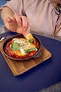 medium sized woman in peach fuzz dress eating Shakshouka in modern restaurant