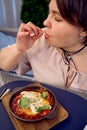 medium sized woman in peach fuzz dress eating Shakshouka in modern restaurant