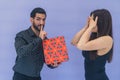 Medium studio shot on blue background of a cuban bearded handsome man holding a colorful present, puting a finger on his