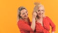Medium studio shot on yellow background of two european blonde-haired women in the 40s wearing similar outfits. One