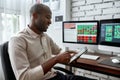 Meet the better future here. Stylish african businessman, trader sitting by desk in front of multiple monitors and using