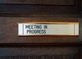 Meeting in progress metal sliding sign on solid dark oak wooden conference room door Royalty Free Stock Photo