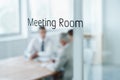 The meeting is in session. Closeup of a glass door reading meeting room with business people blurred in the room behind. Royalty Free Stock Photo