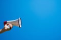 Megaphone in a female hand on a blue background. No people. Cropped photo. A woman holds a sound amplifier against the