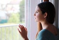 Melancholic sad young woman looking through the window at home in a rainy day, focus on model eyes, indoor photo Royalty Free Stock Photo