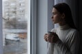 Melancholic young woman with drink looking out of window on rainy day, space for text. Loneliness concept Royalty Free Stock Photo