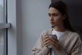 Melancholic young woman with drink looking out of window on rainy day, space for text. Loneliness concept Royalty Free Stock Photo