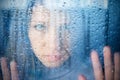 Melancholy and sad young woman at the window in the rain