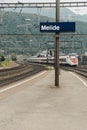 Melide station, blue sign with the name of the station. The high speed train is coming