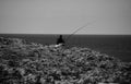 MELLIEHA, MALTA - Oct 12, 2014: A man fishing alone in peace on a cliff in Malta, looking towards the horizon