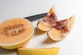 Melon slices with cured ham slices on top with a half melon and knife