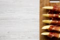 Melon slices wrapped in prosciutto on bamboo board over white wooden background, top view. Close-up. From above, overhead, flat la Royalty Free Stock Photo