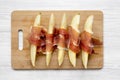 Melon slices wrapped in prosciutto on bamboo board over white wooden background, top view. Close-up. From above, overhead Royalty Free Stock Photo