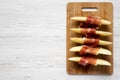 Melon slices wrapped in prosciutto on bamboo board over white wooden background, top view. Closeup. From above, overhead, flat lay Royalty Free Stock Photo