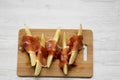 Melon slices wrapped in prosciutto on bamboo board over white wooden table, overhead view. From above, top view. Royalty Free Stock Photo