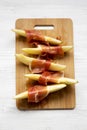 Melon slices wrapped in prosciutto on bamboo board over white wooden table, overhead view. Closeup. From above Royalty Free Stock Photo