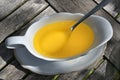 Melted butter in a white sauce boat on a wooden garden table, high angle view from above