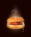 Melted cheese flows from a hot cheeseburger close up on a dark background. Freshly baked cheeseburger with steam smoke on a black